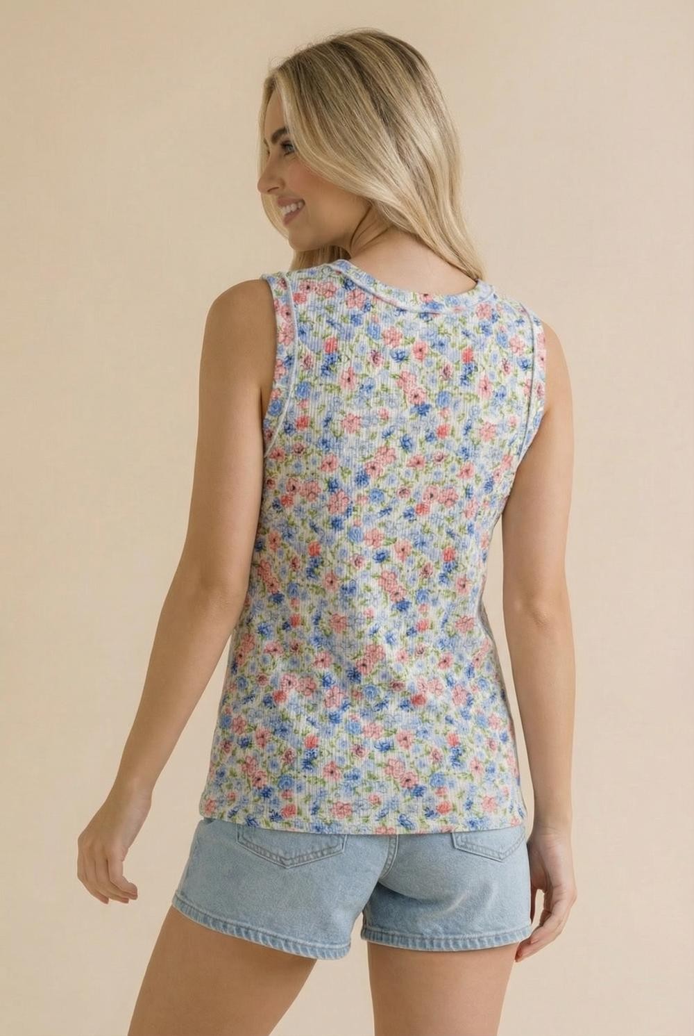 woman wearing a floral print sleeveless top with a gray background and denim shorts, viewed from the back