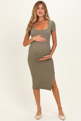 woman wearing an olive green ribbed maternity dress with short sleeves and a side slit, holding her baby bump