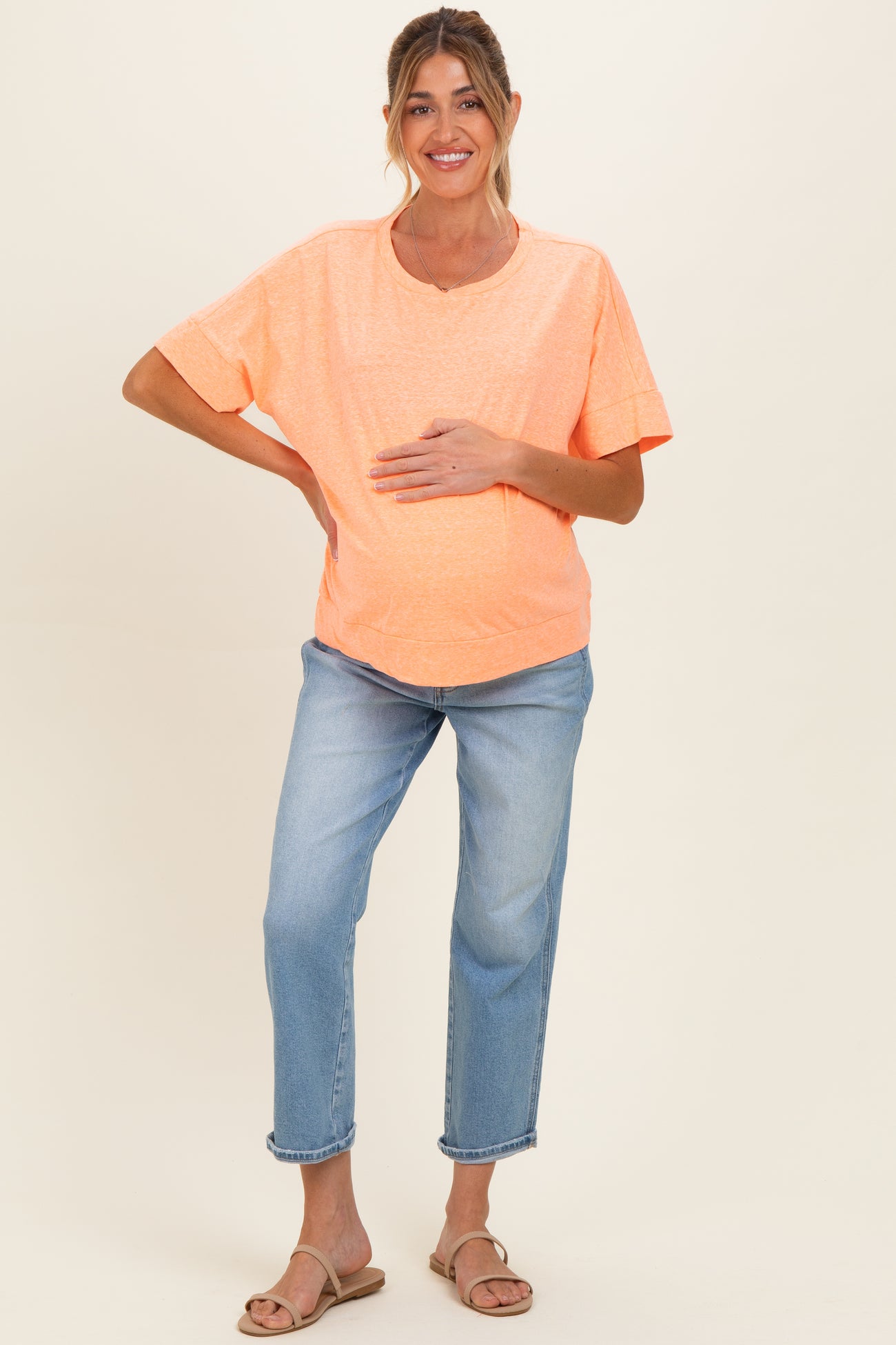 woman wearing a bright orange short sleeve maternity top and blue jeans, holding her baby bump