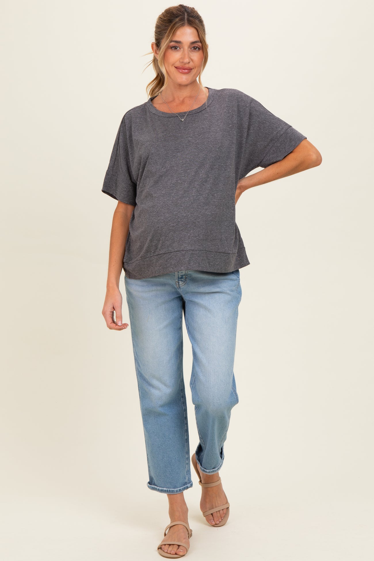 woman wearing a gray short sleeve maternity top and light blue high-waisted jeans, showcasing her baby bump