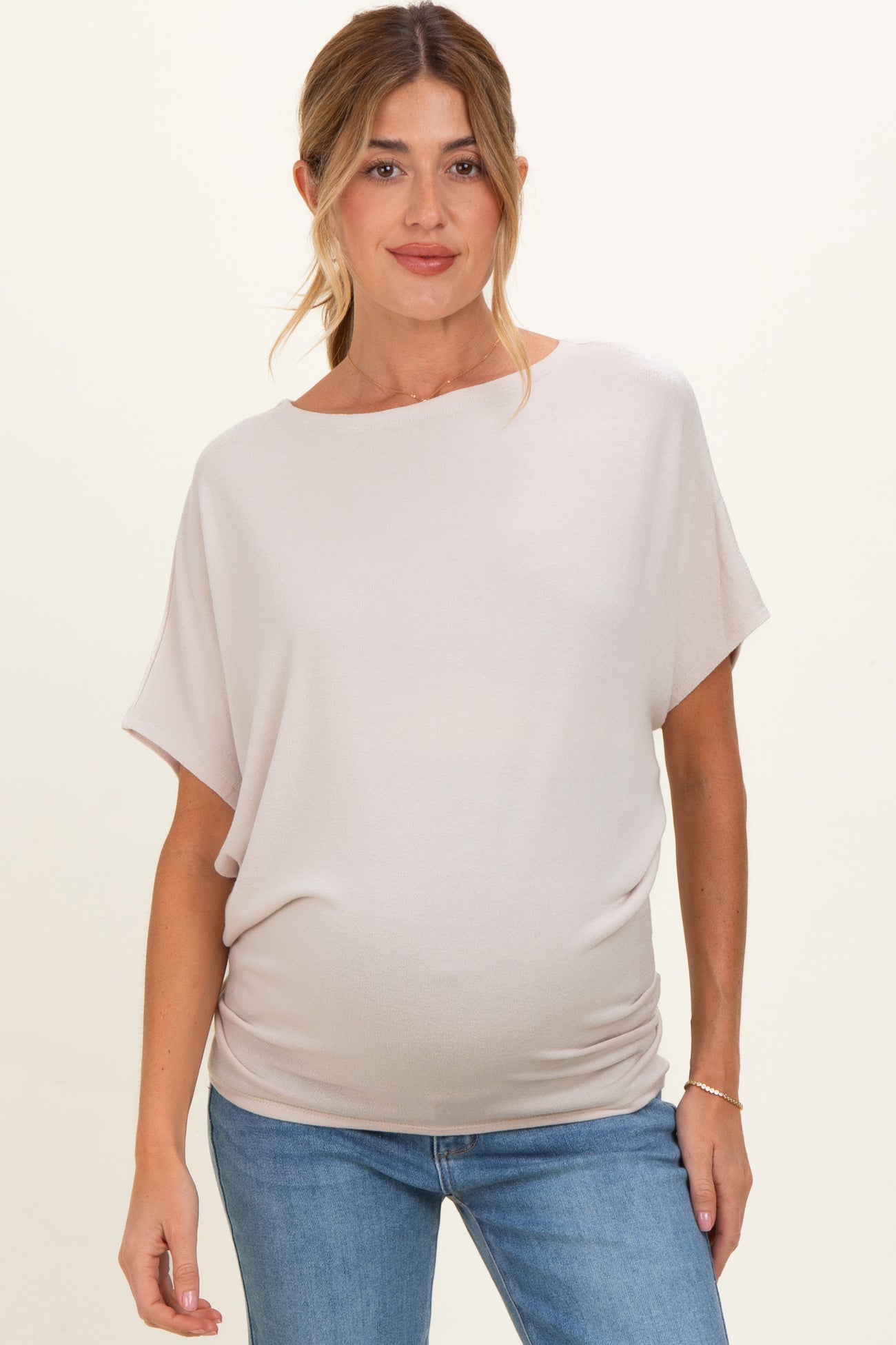 woman wearing a light beige maternity top with a relaxed fit and gathered sides, showing her baby bump