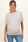 woman wearing a light beige maternity top with a relaxed fit and gathered sides, showing her baby bump