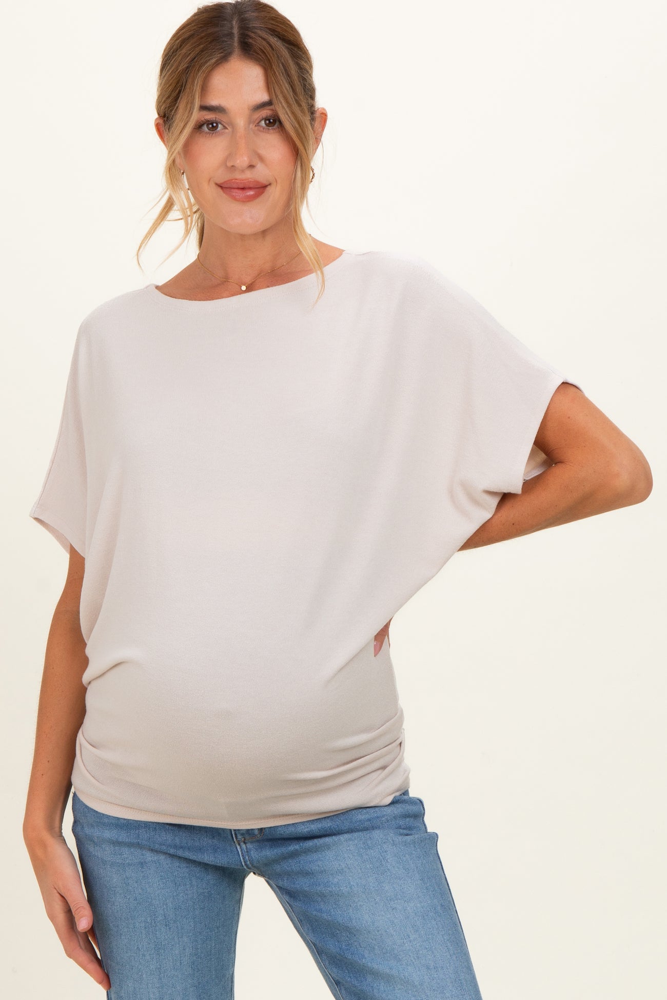 woman wearing a light beige maternity top with loose sleeves and a visible baby bump, paired with blue jeans
