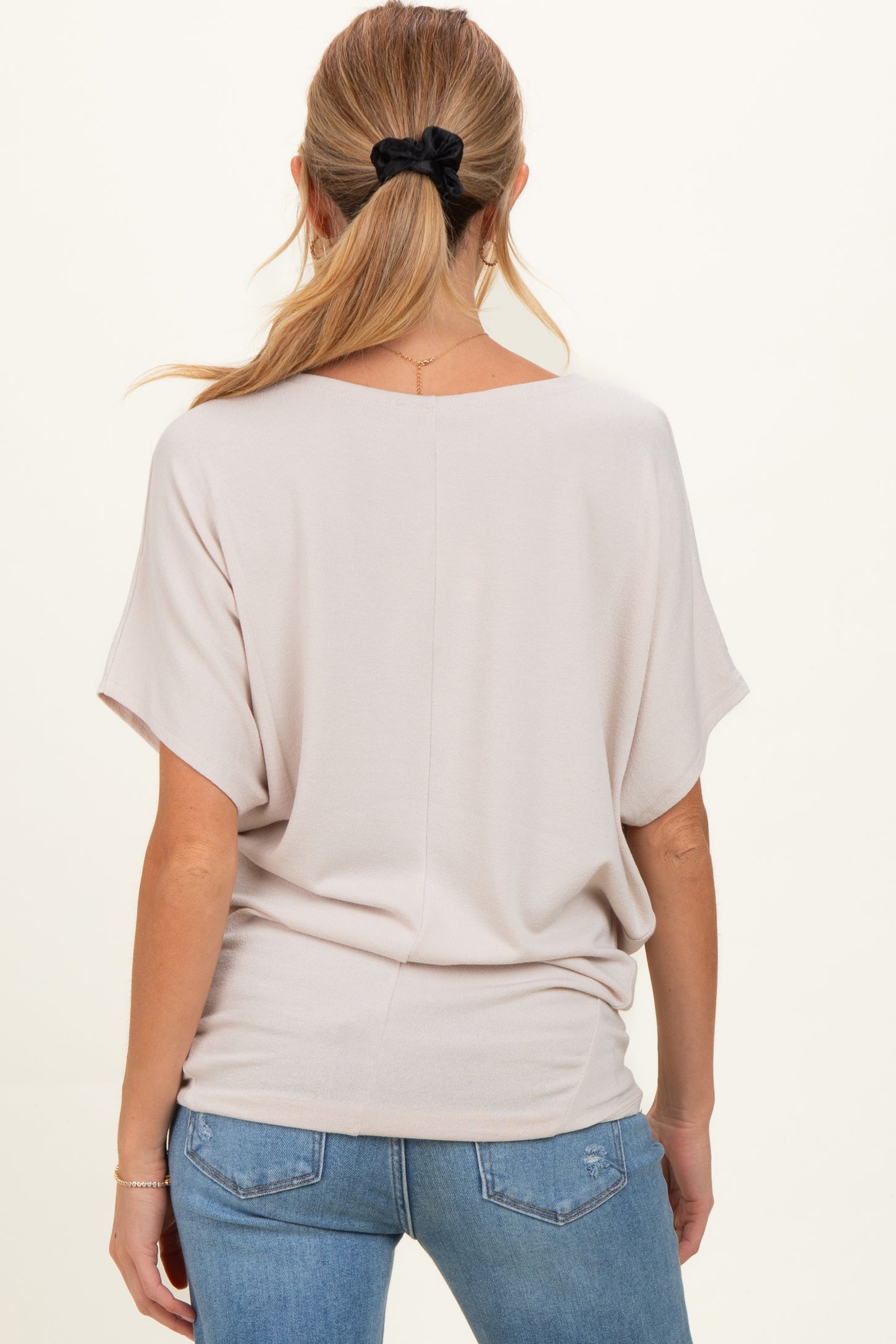 woman wearing a light beige maternity top with short sleeves and a relaxed fit, showing her back and styled with jeans