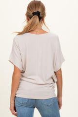 woman wearing a light beige maternity top with short sleeves and a relaxed fit, showing her back and styled with jeans