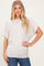 woman wearing a soft beige oversized short sleeve top and blue jeans, standing with one hand on her hip