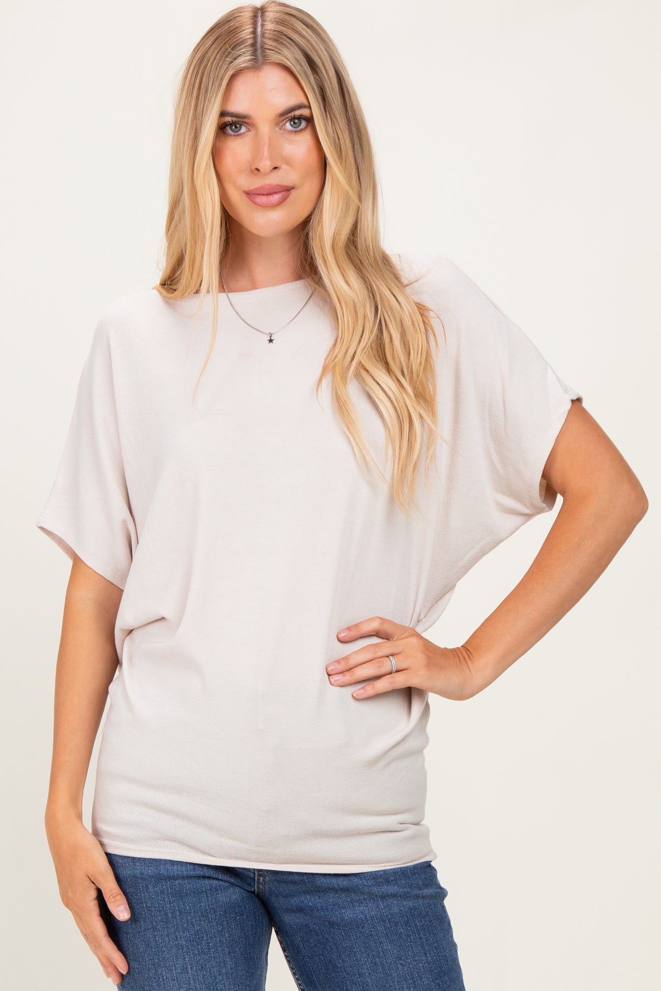 woman wearing a soft beige oversized short sleeve top and blue jeans, standing with one hand on her hip