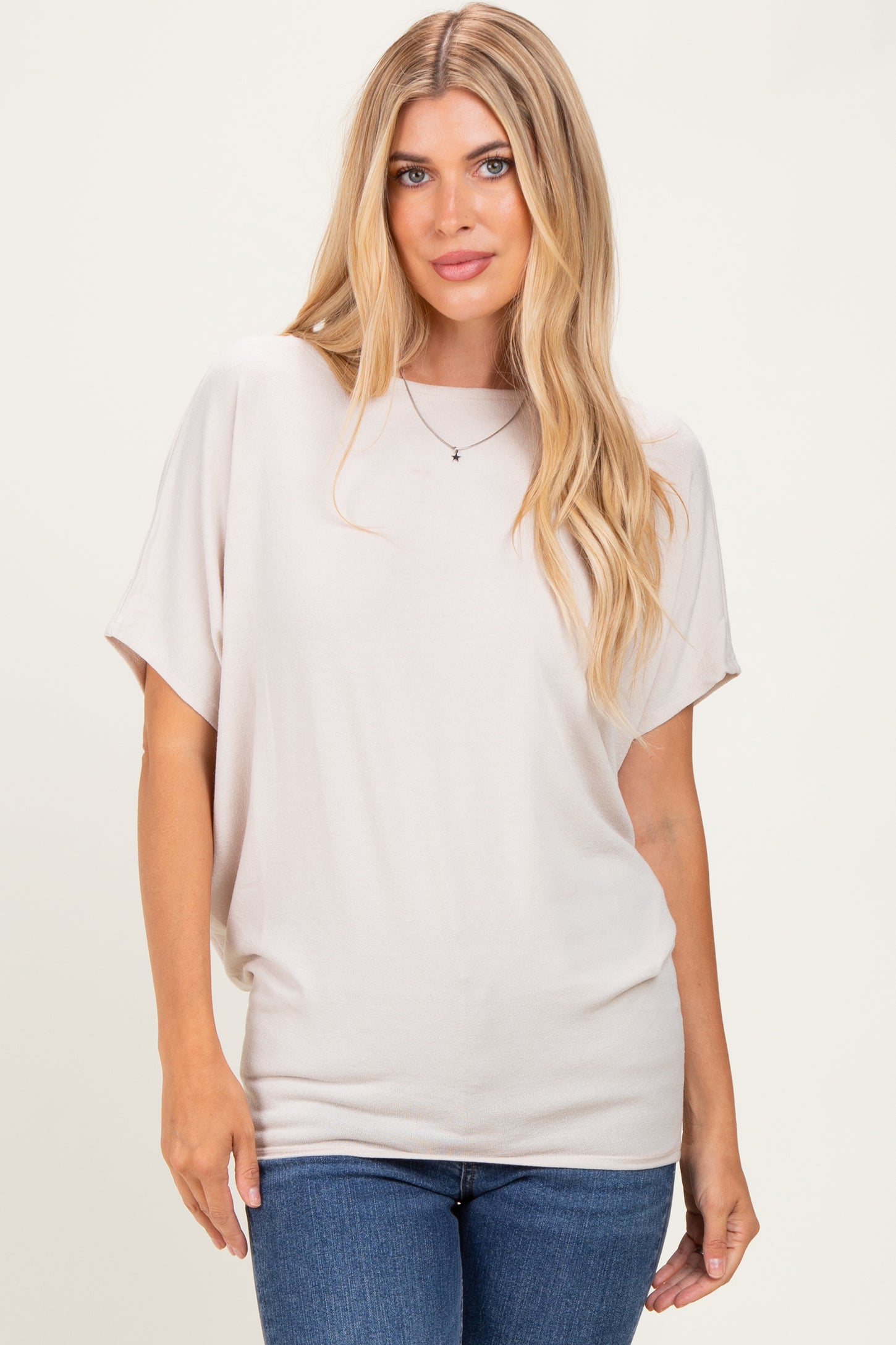 woman wearing a light beige oversized short sleeve top paired with blue jeans