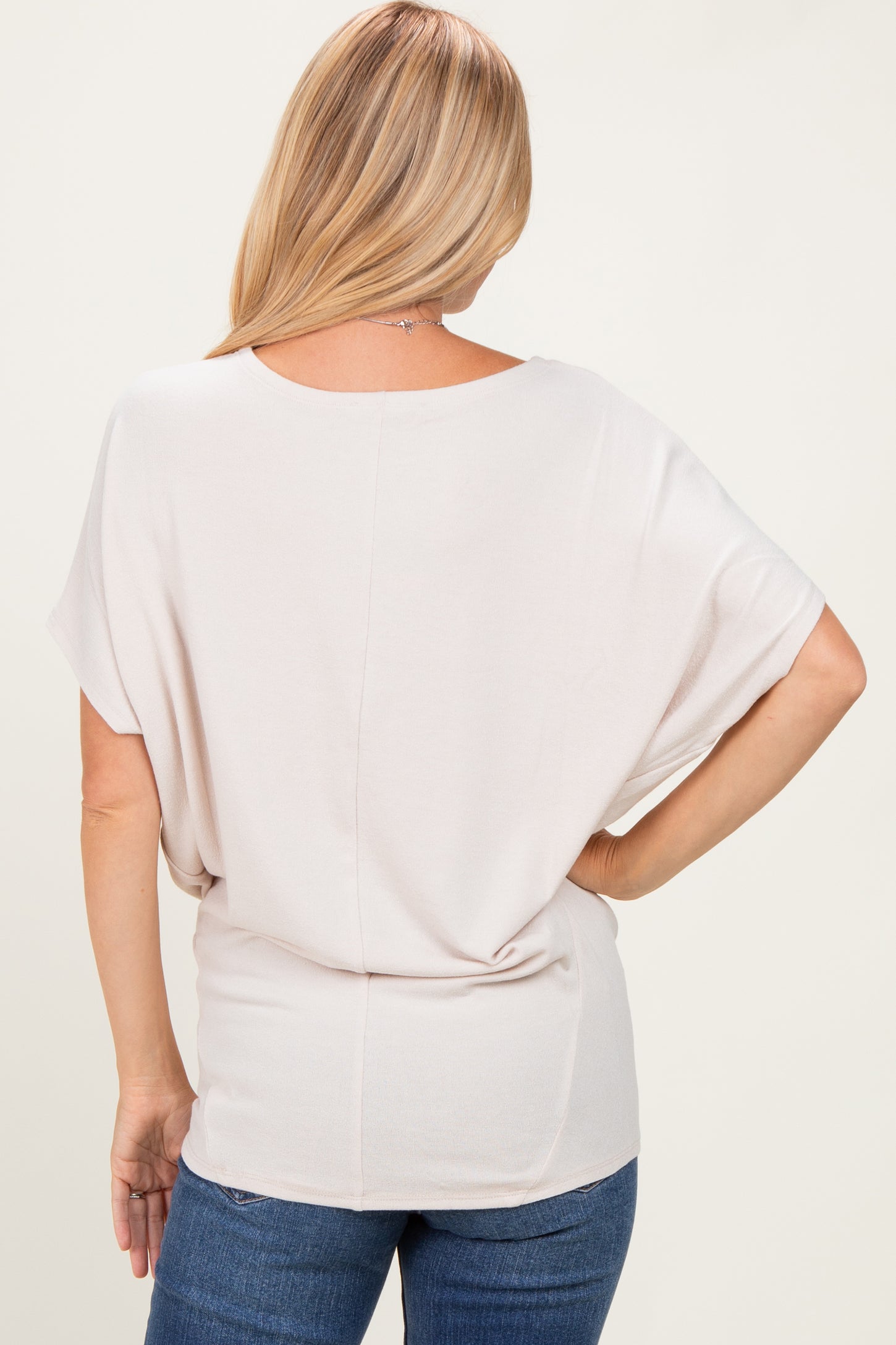 woman wearing a light beige loose-fitting top with short sleeves and a relaxed back style