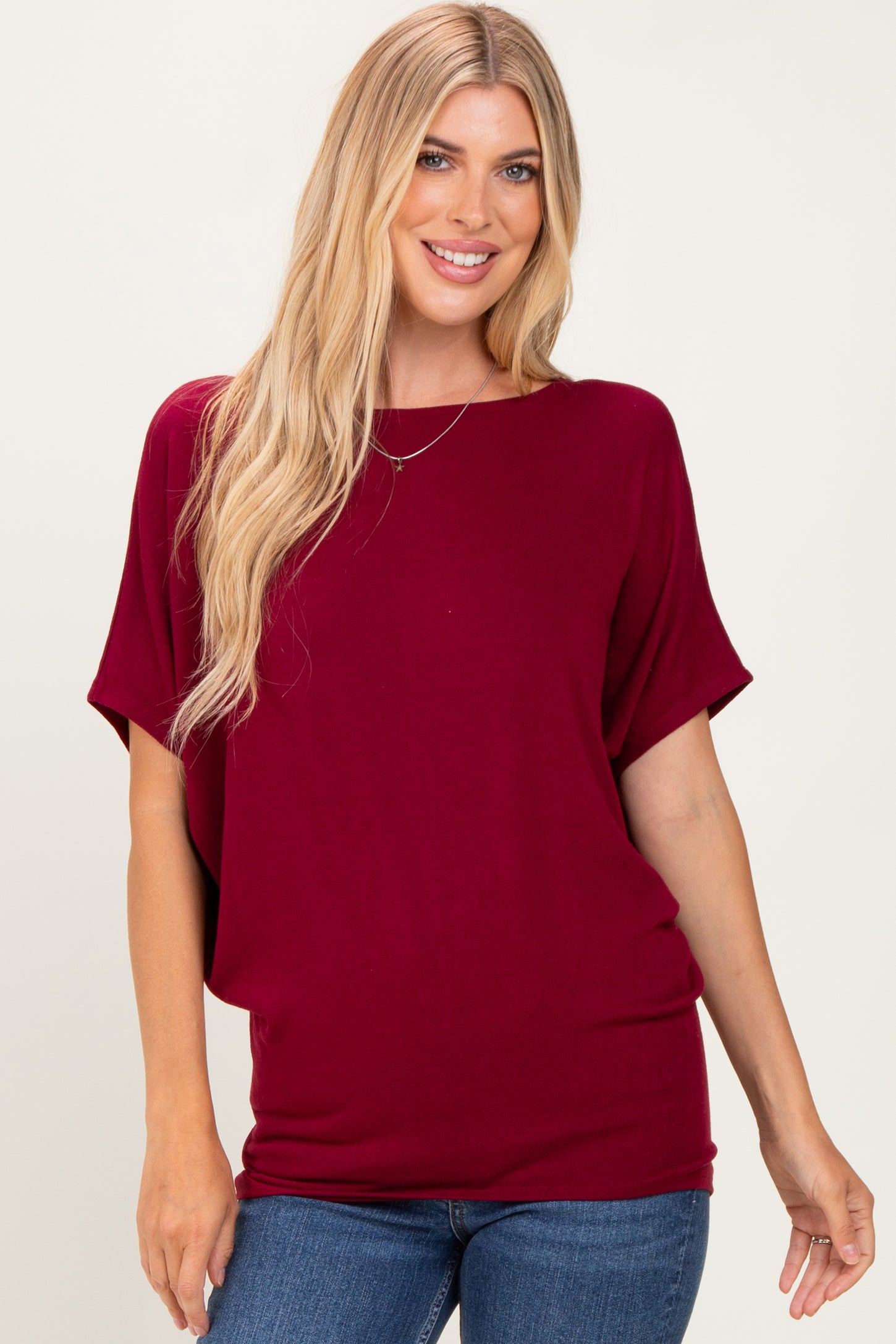 woman wearing a maroon oversized short sleeve top with a round neckline and relaxed fit paired with blue jeans