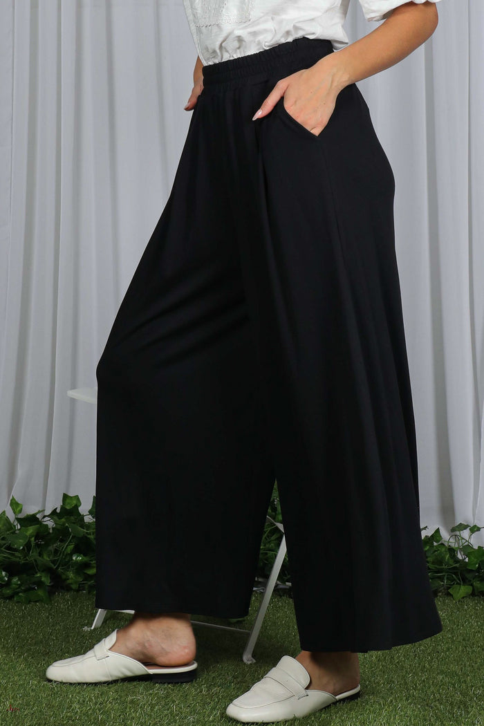 woman wearing black wide-leg pants with elastic waistband and side pockets, styled casually with white slippers
