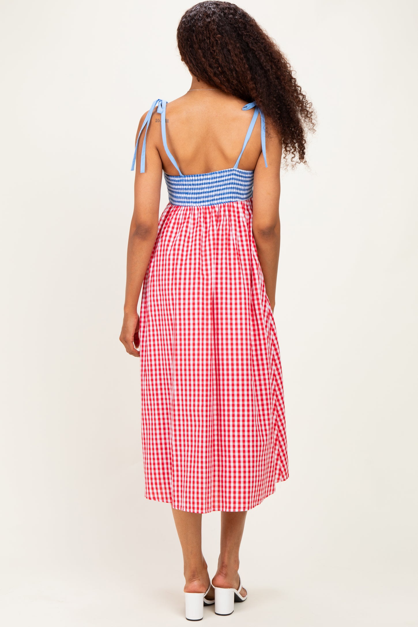 woman wearing a back view of a red and white gingham midi dress with blue smocking and tie straps