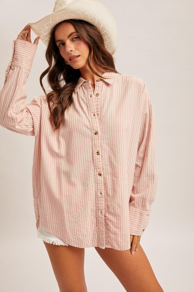 woman wearing a pink and white striped button-up shirt with rolled sleeves and a straw hat