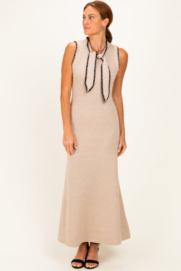 woman wearing a beige sleeveless maxi dress with a black tie and ribbed texture, standing on a light background