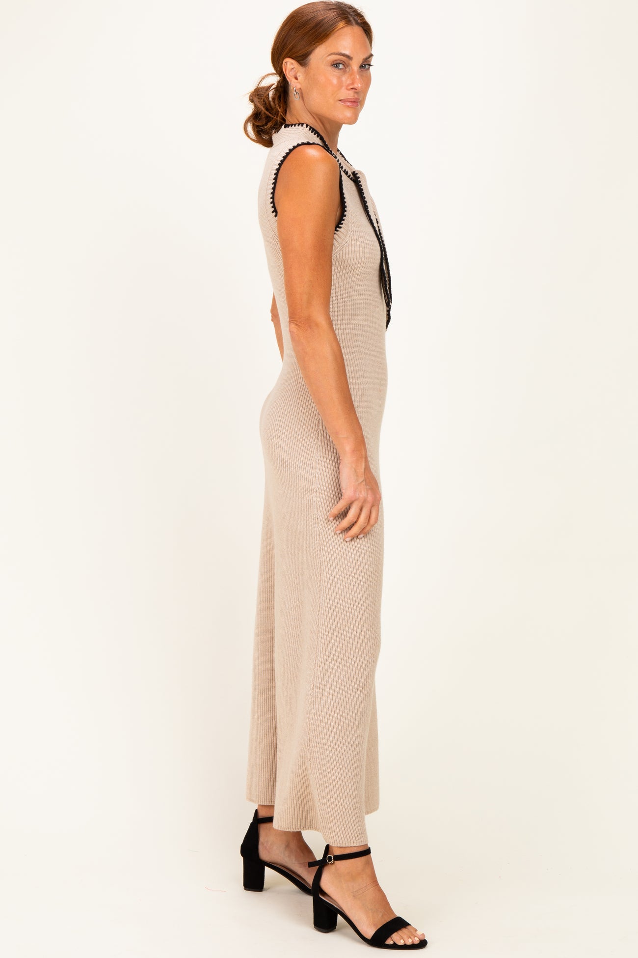 woman wearing a beige ribbed knit sleeveless dress with black trim and strappy black heels