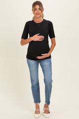 woman wearing a black maternity top with puff sleeves and a baby bump, paired with light blue distressed jeans