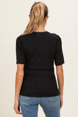 woman wearing a black ribbed maternity top with short sleeves and ruched detail at the waist