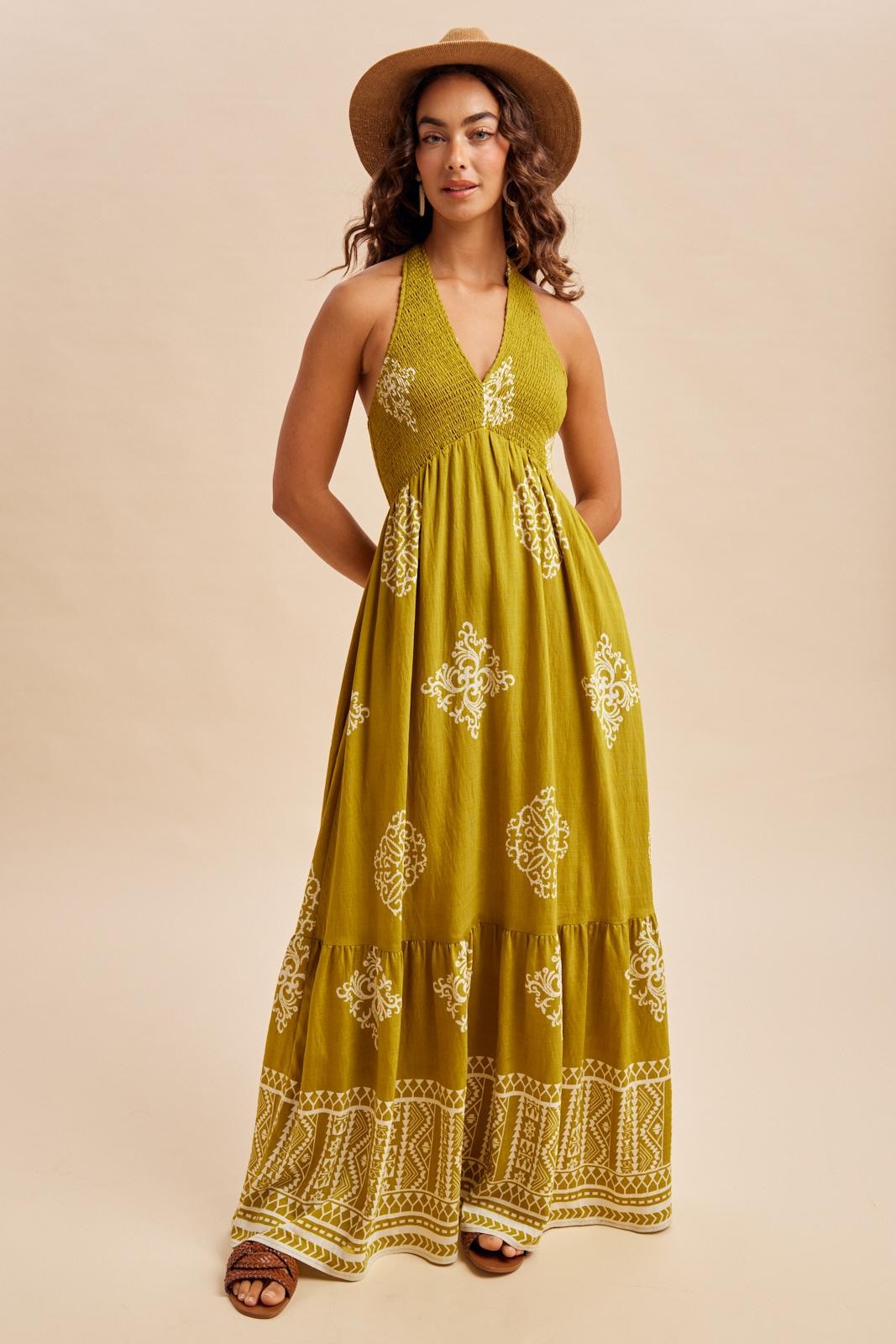 woman wearing a green floral patterned maxi dress with halter neckline and tiered skirt, styled with a straw hat