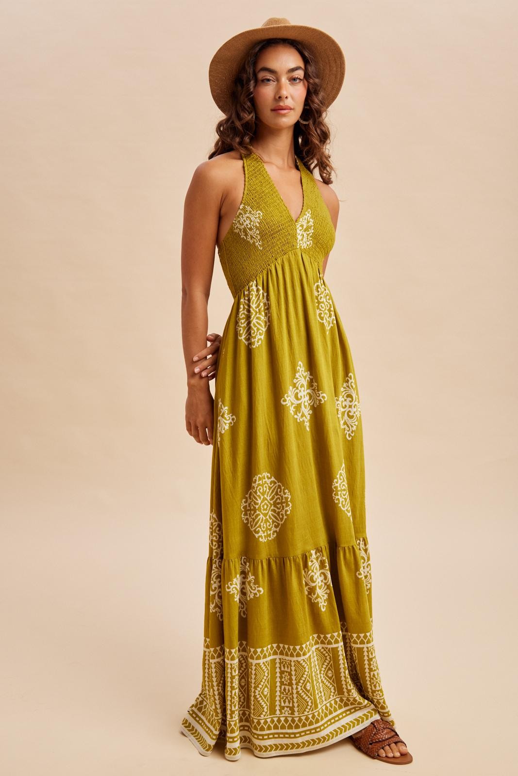 woman wearing a mustard yellow maxi dress with white embroidered details and a wide-brimmed hat