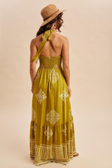 woman wearing a mustard yellow maxi dress with intricate white patterns and a halter neck tie, seen from the back
