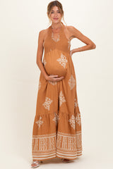 woman wearing a brown halter-neck maternity maxi dress with smocking and boho patterns, holding her baby bump