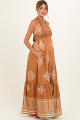 woman wearing a brown patterned maternity maxi dress with an empire waist and pockets, showcasing a baby bump