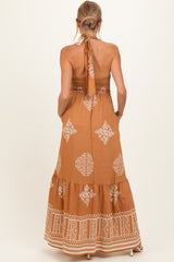 woman wearing a brown patterned maternity maxi dress with a halter neck and smocked bodice, showing a baby bump