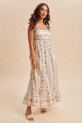 woman wearing a floral print maxi dress with thin straps and a tiered hem, standing against a neutral background