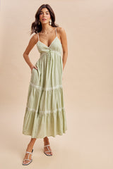 woman wearing a light green maxi dress with a tie front, lace trim, and pockets, standing against a neutral background