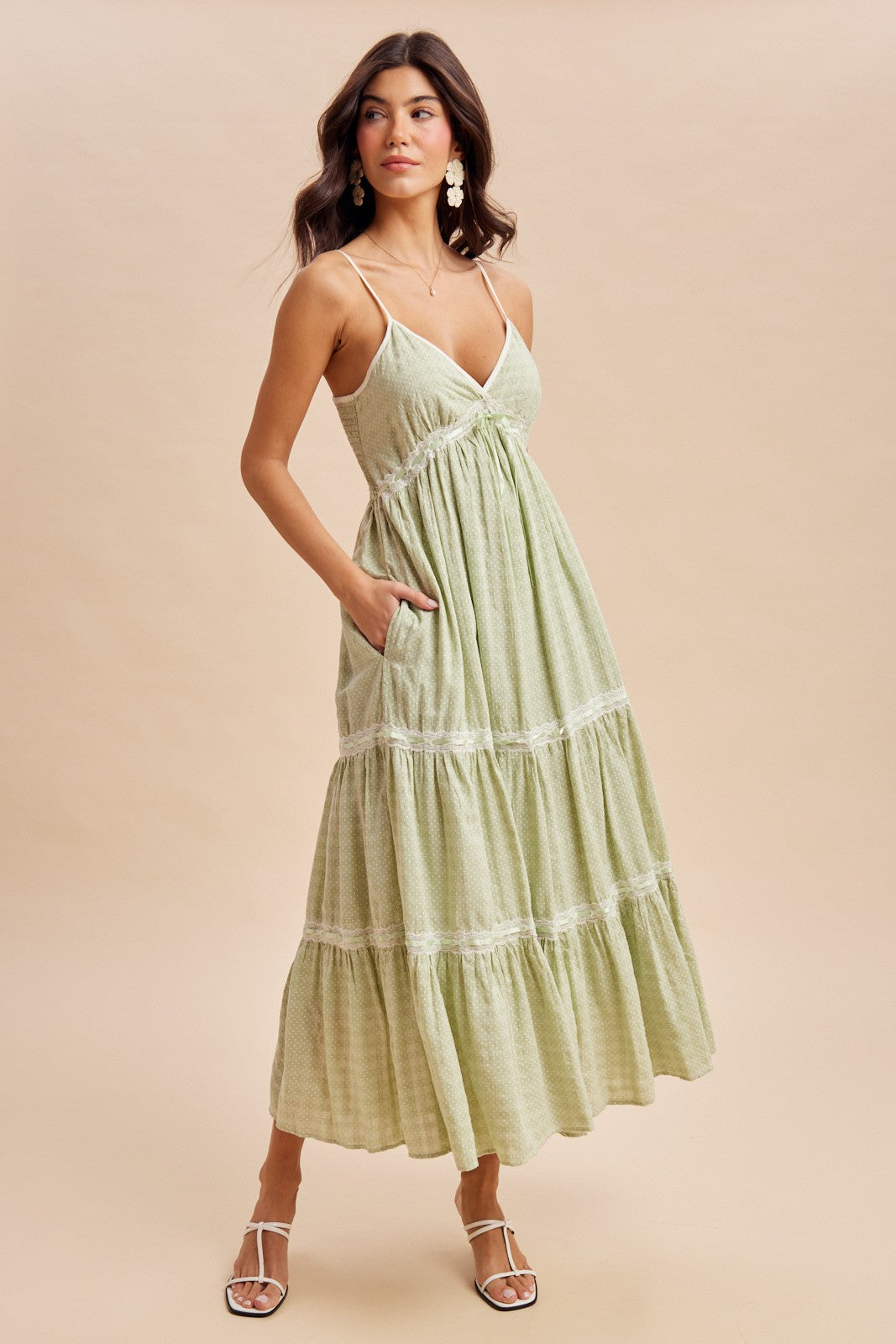 woman wearing a light green tiered maxi dress with spaghetti straps and pockets, standing on a tan background