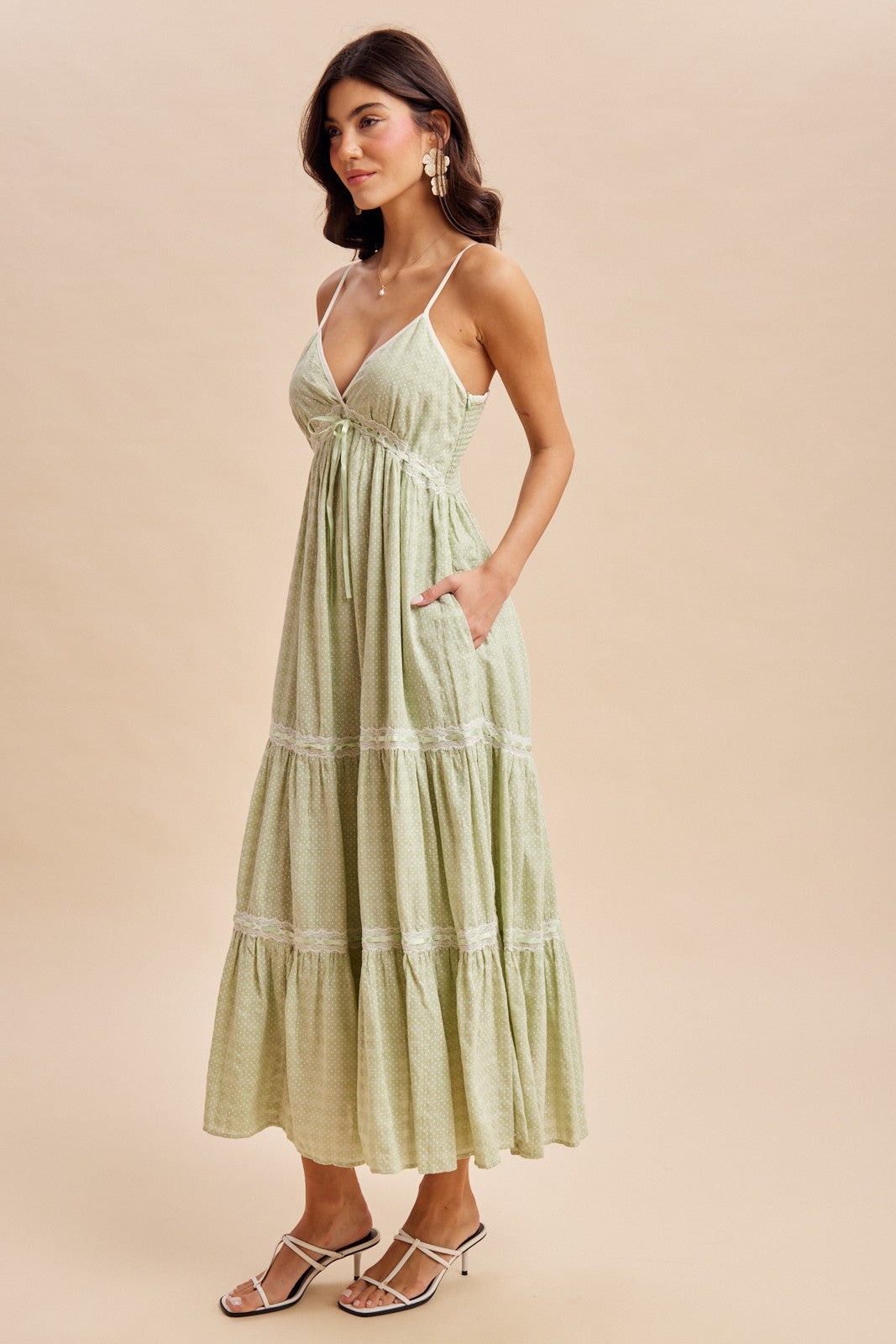 woman wearing a green polka dot maxi dress with adjustable straps and pockets in a tiered design