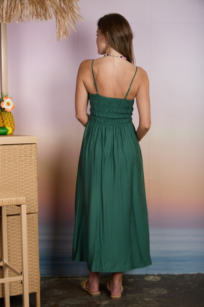 woman wearing a green smocked maxi dress with thin straps, standing with her back to the camera