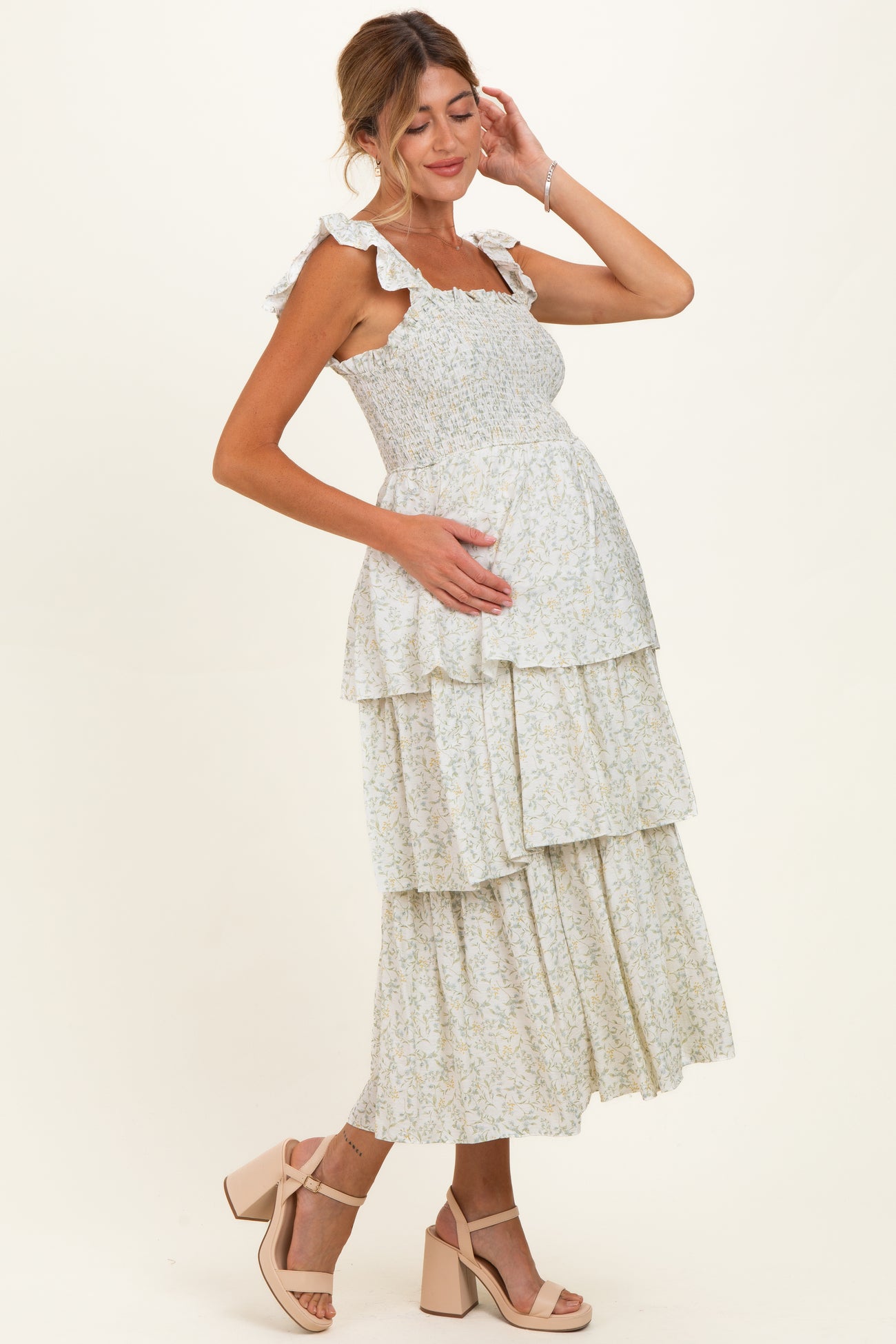 woman wearing a floral maternity maxi dress with tiered layers and ruffled straps, holding her baby bump
