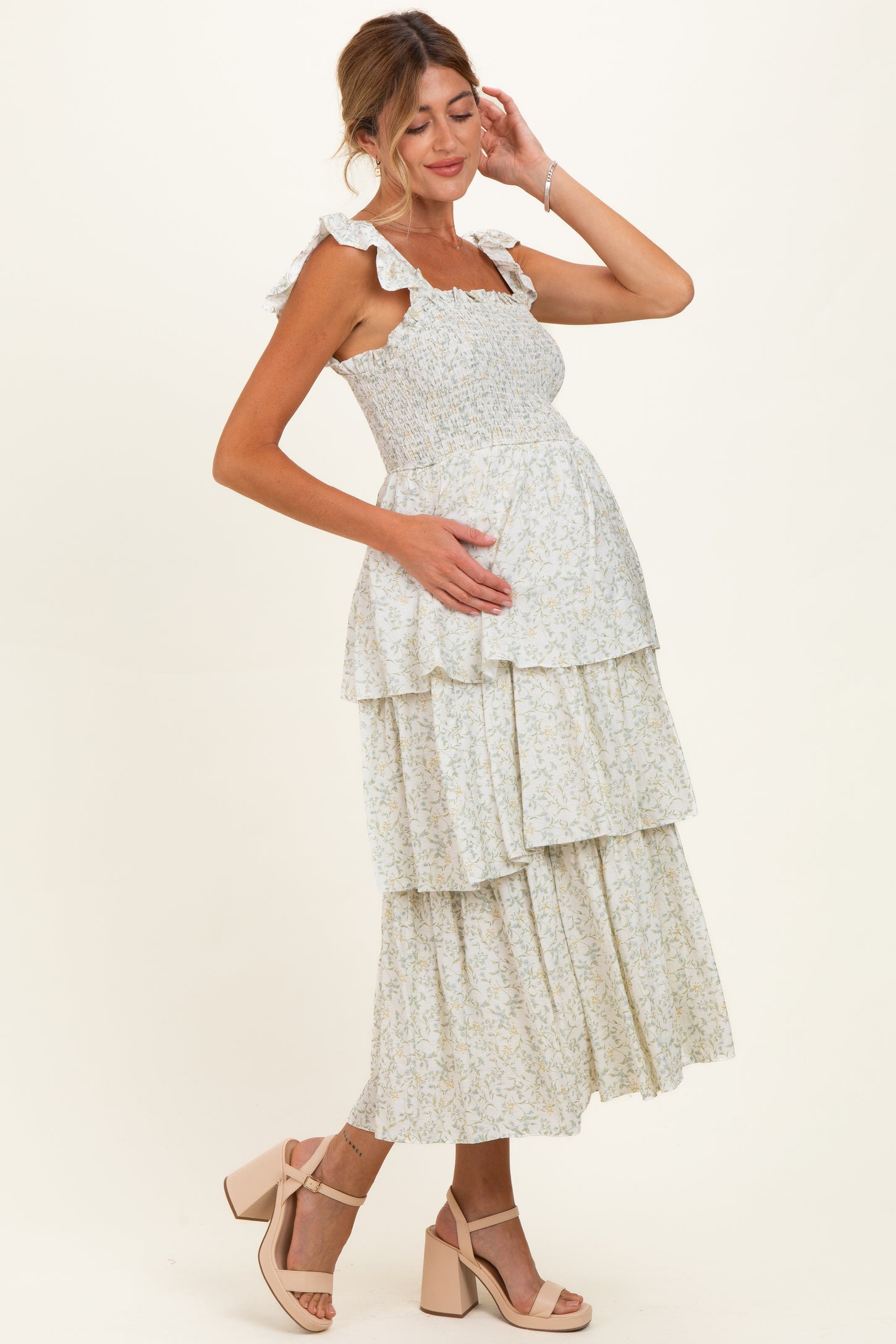 woman wearing a floral maternity maxi dress with tiered layers and ruffled straps, holding her baby bump