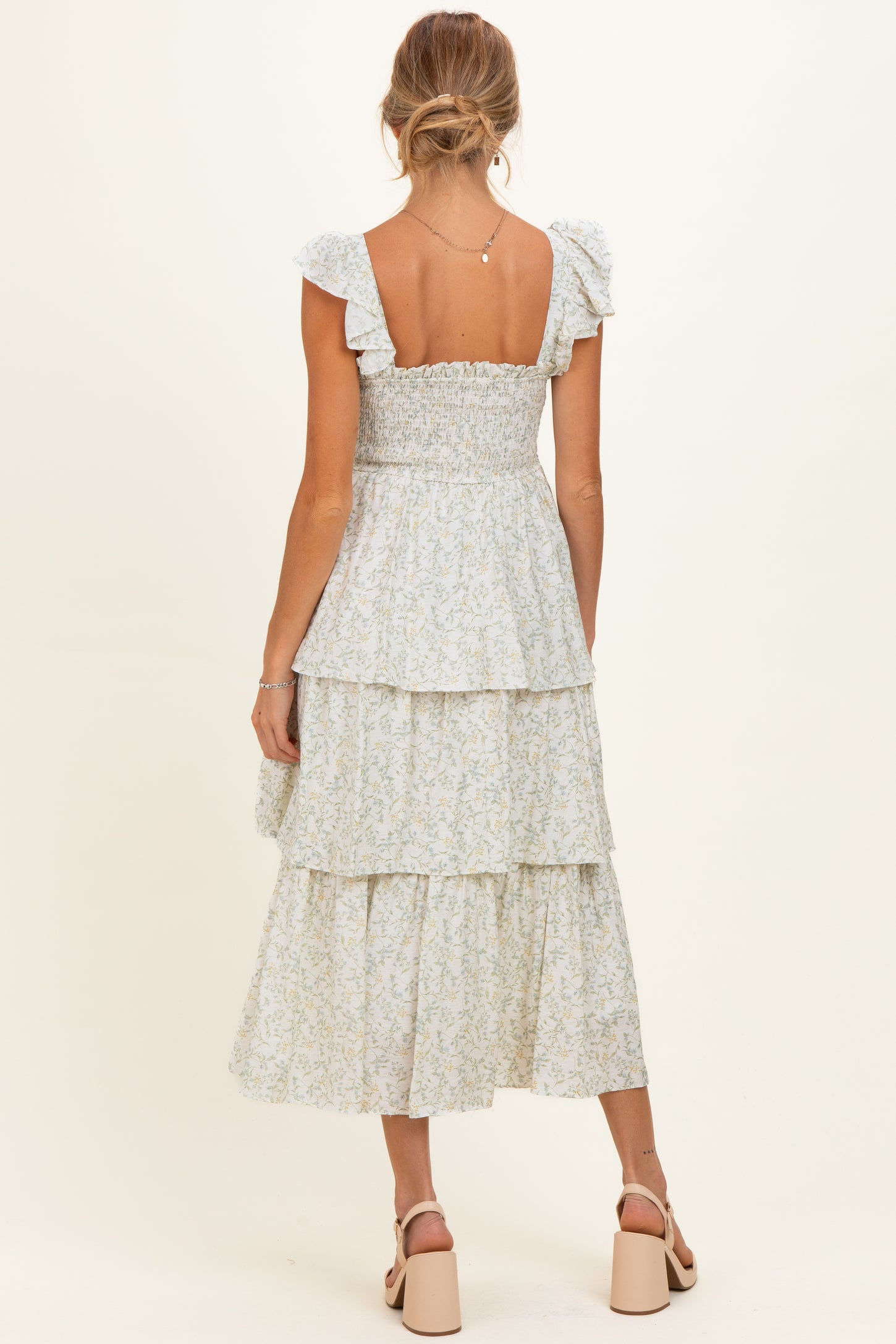 woman wearing a light blue floral maternity dress with ruffled straps and a tiered skirt, showing off her baby bump