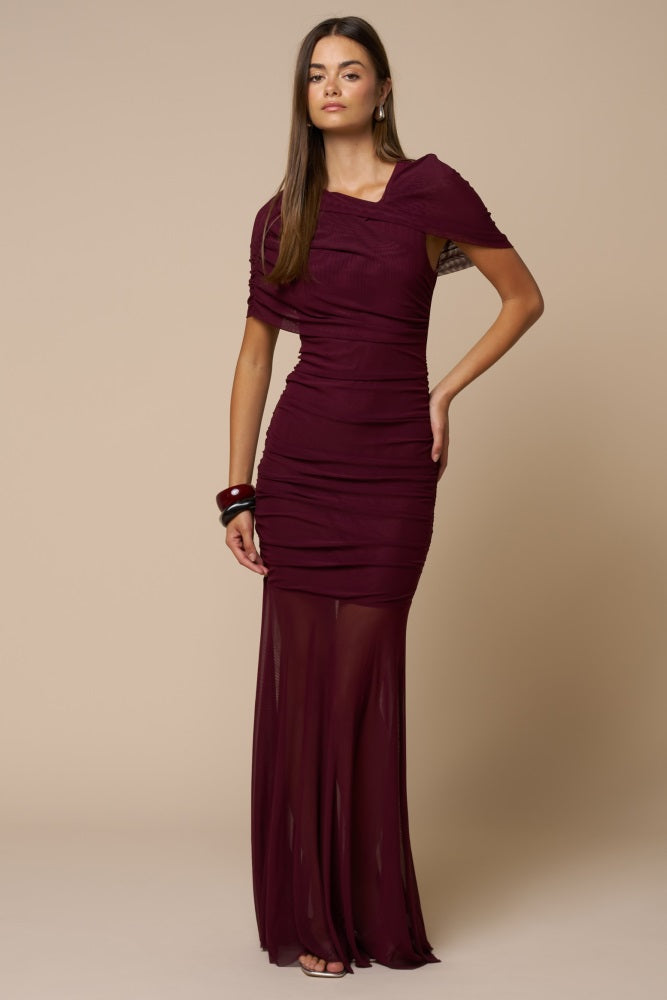 woman wearing a burgundy off-shoulder ruched evening gown with a sheer skirt and stylish accessories