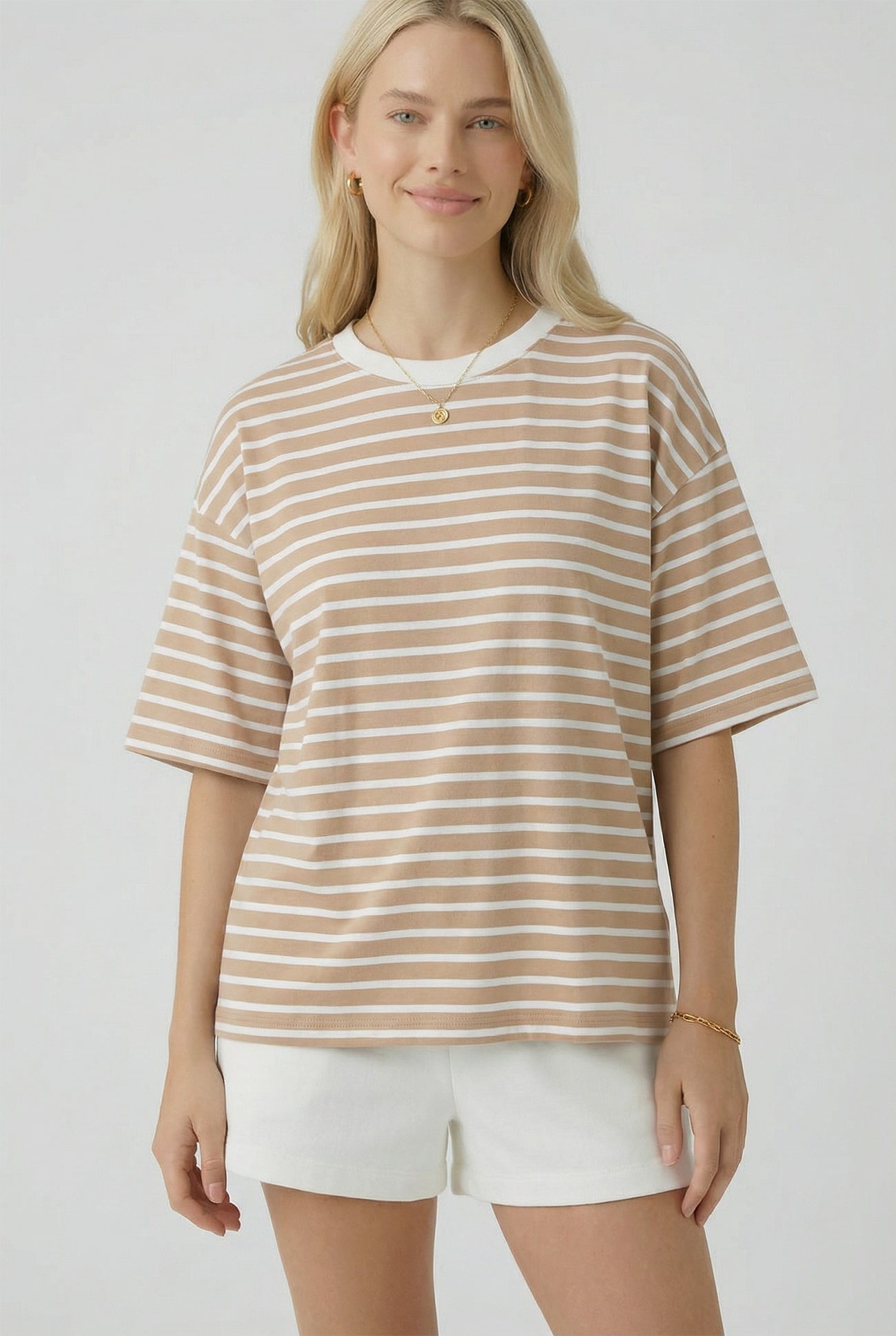 woman wearing a beige and white striped oversized t-shirt with short sleeves and standing with a slight smile