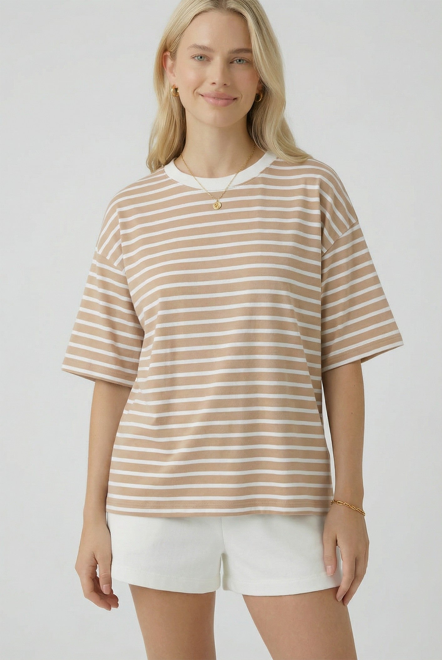woman wearing a beige and white striped oversized t-shirt with short sleeves and standing with a slight smile