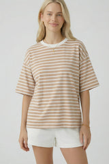 woman wearing a beige and white striped oversized t-shirt with short sleeves and standing with a slight smile