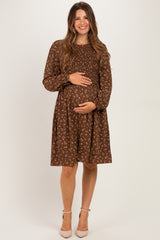 woman wearing a brown floral smocked maternity dress, holding her baby bump