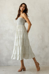 woman wearing a light floral midi dress with a smocked bodice and spaghetti straps, posing with a smile
