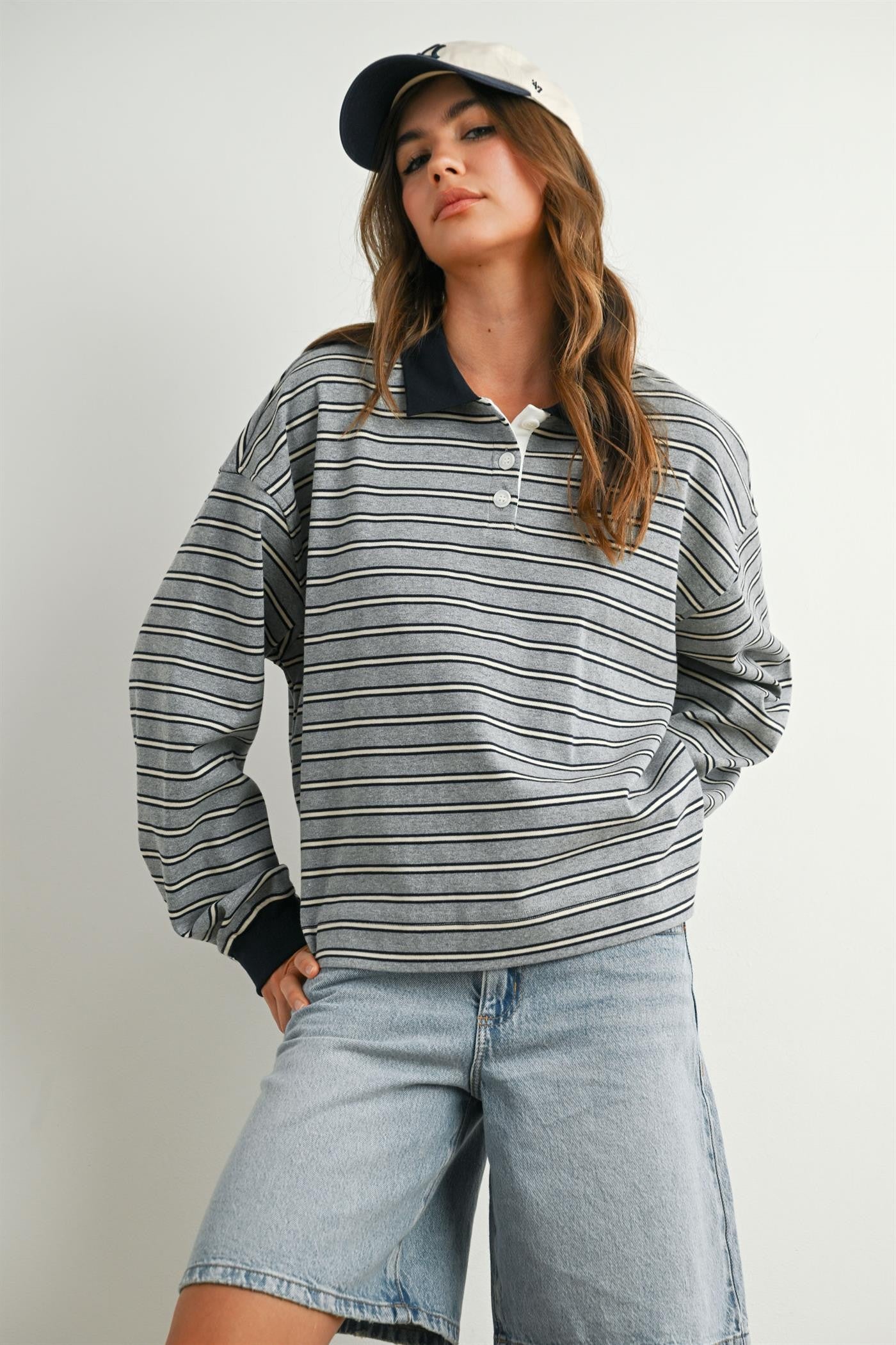 woman wearing a striped gray and navy long sleeve polo shirt with oversized sleeves and denim shorts