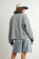 woman wearing a gray striped oversized sweatshirt with black cuffs and denim shorts, seen from the back
