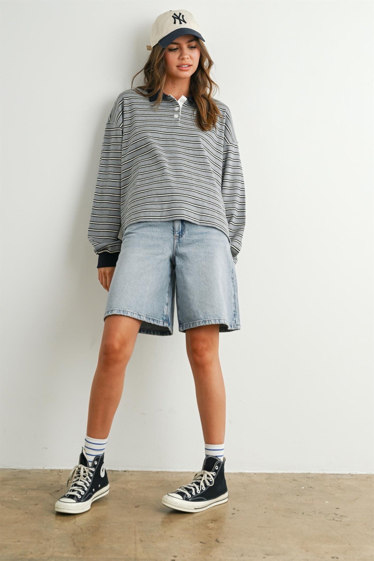 woman wearing a gray and white striped long sleeve polo shirt with denim bermuda shorts and black sneakers