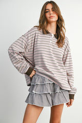 woman wearing a light pink and brown striped oversized sweatshirt and a black and white gingham ruffled skirt