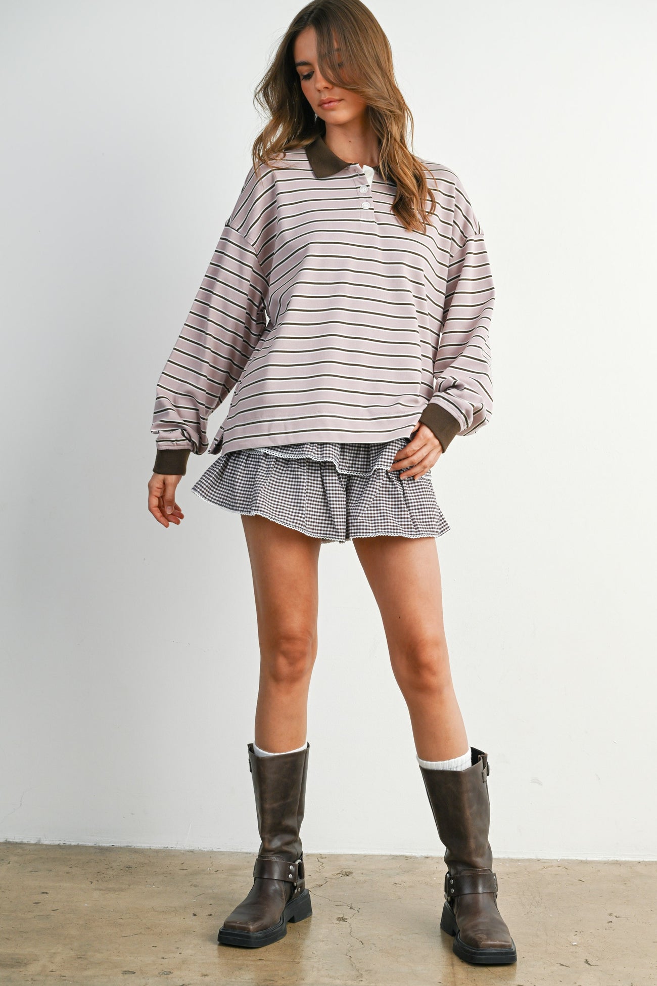 woman wearing a light pink striped oversized polo shirt with brown accents and a checkered mini skirt, paired with brown knee-high boots