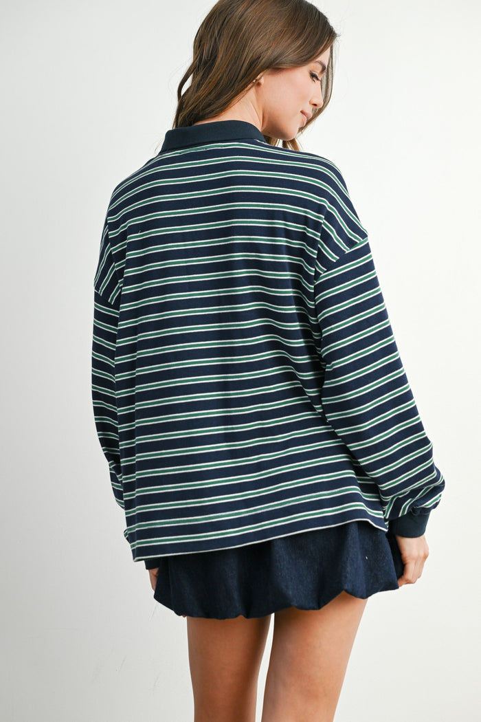 woman wearing a navy blue and green striped long sleeve shirt, viewed from the back with a layered look over a dark skirt