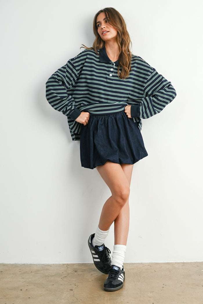 woman wearing a navy and green striped oversized polo sweater with a dark skirt and black sneakers