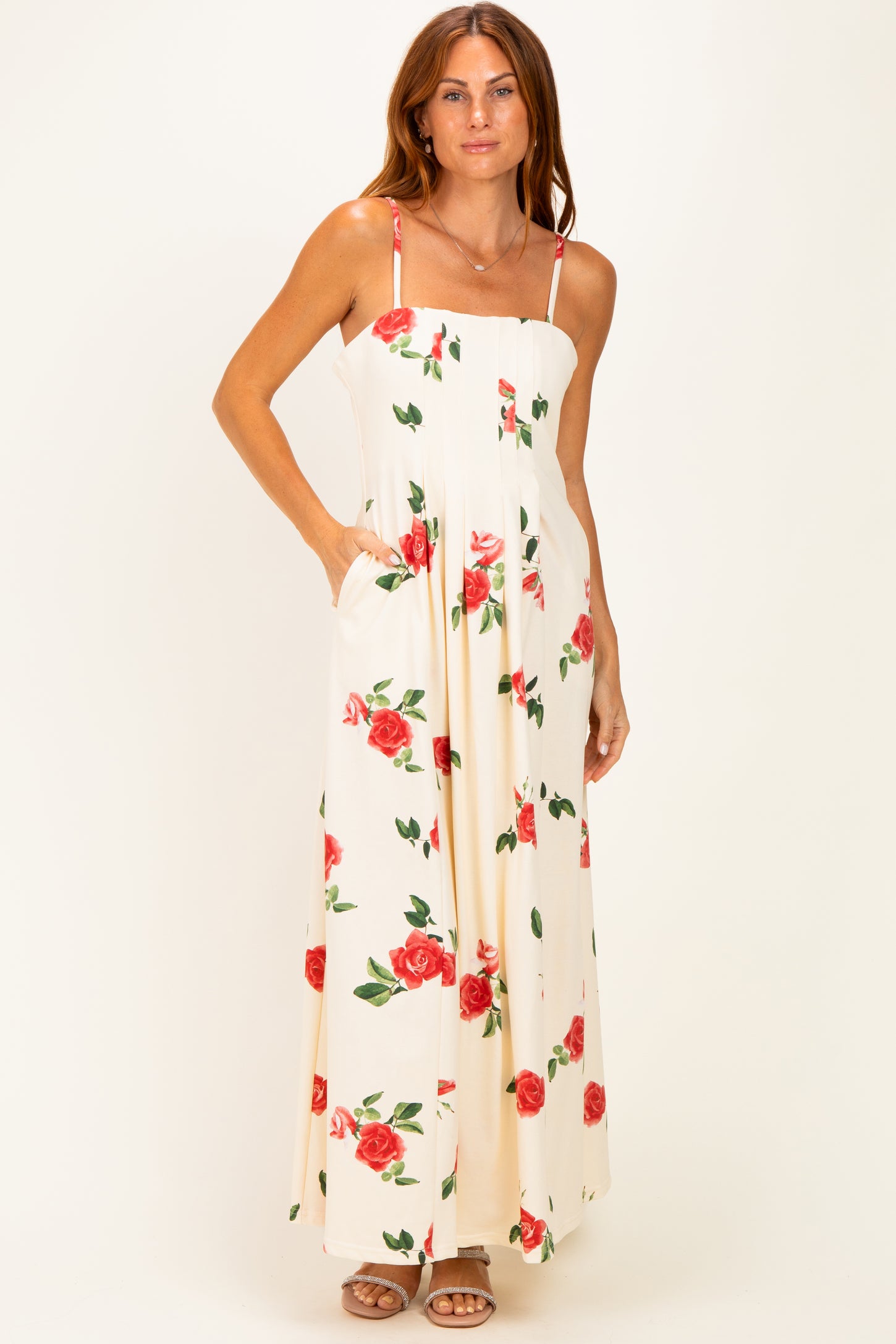 woman wearing a white maxi dress with red rose prints and pockets, featuring thin straps and a fitted bodice