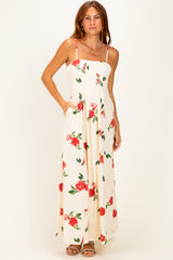 woman wearing a white maxi dress with red rose prints and pockets, featuring thin straps and a fitted bodice